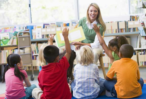 Teacher reads to class raising hands